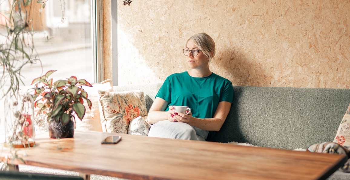 Kvinne sitter på kafe med en kopp kaffe og ser ut av vinduet