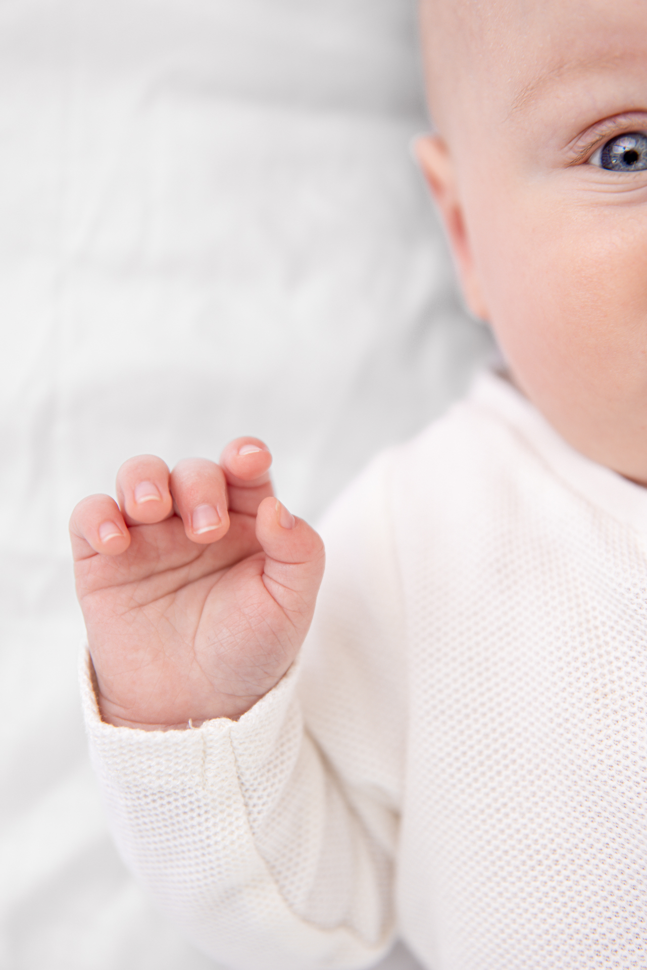 Baby på 6 måneder ligger på rygg, utsnitt av bilde viser ene øyet og hånden til babyen