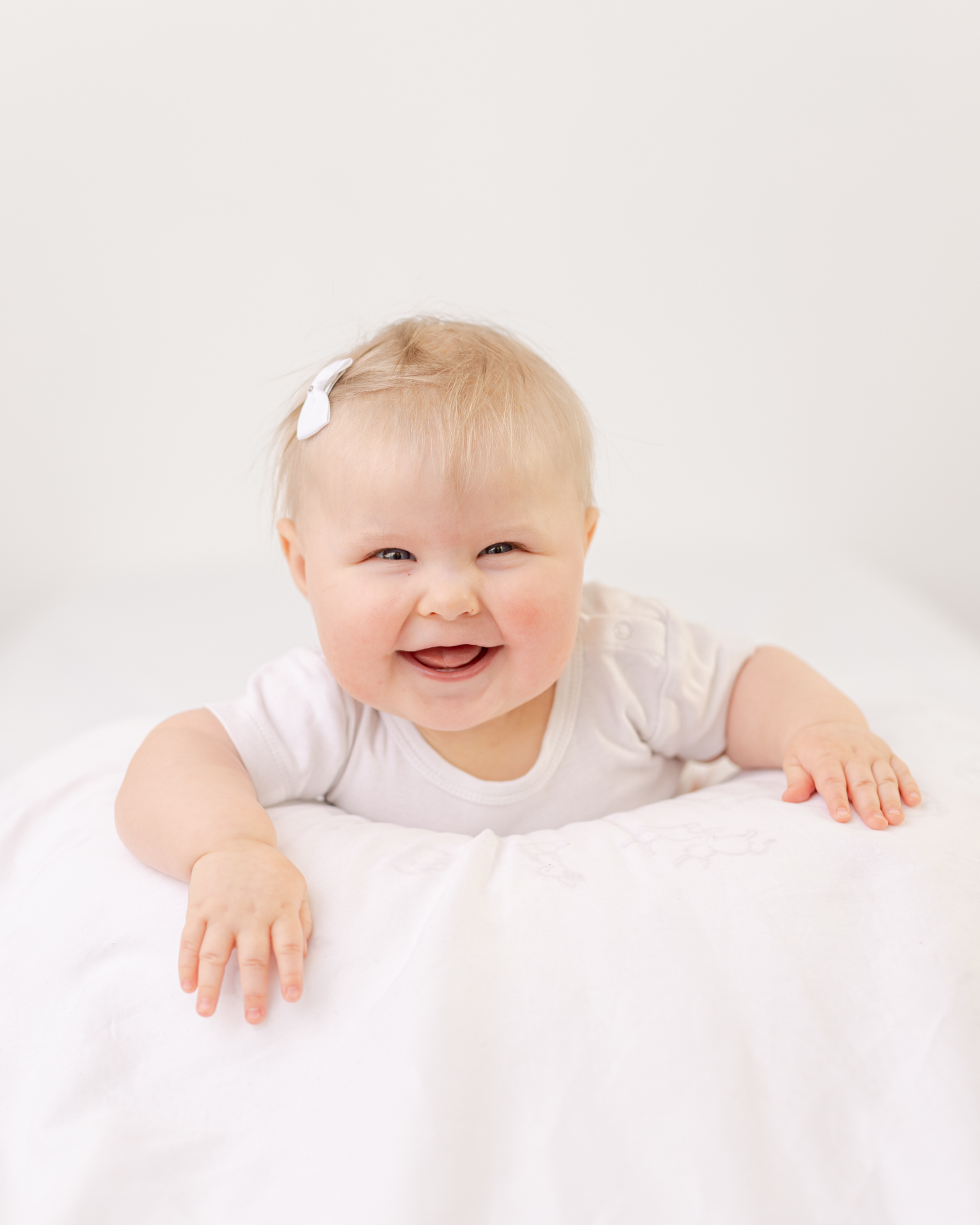 Portrett av en baby som ligger på magen og smiler mot kamera